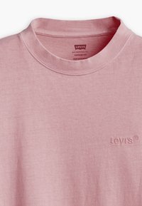Světle růžové tričko Levi's s kulatým výstřihem a jemnou strukturou. Obsahuje decentní vyšitý logo na hrudi. Design v vintage střihu.
