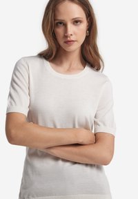Hvid strik kortærmet sweater med rund halsudskæring. Blød tekstur og ribstrikkede manchetter. Tætsiddende design, der fremhæver formen.