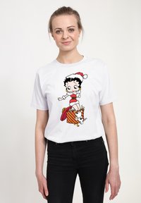 Vit T-shirt med en tecknad design av en karaktär i röd och vit outfit med en presentask, mot en enfärgad bakgrund.