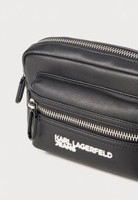 Borsa in pelle sintetica nera con numerosi scomparti con zip, accessori in tono argento e testo impresso "KARL LAGERFELD JEANS."
