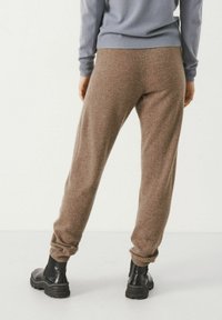 Pantalones de chándal marrones hechos de un tejido suave y texturizado, con puños elásticos, combinados con botas negras hasta el tobillo para un look casual.