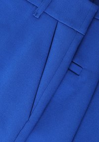 Blue fabric of tailored pants featuring a smooth texture and creased design. Includes side pockets and a flat front.