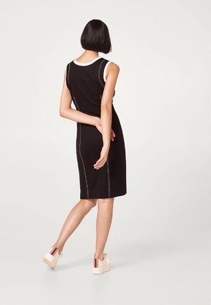 Sort ærmeløs kjole med kontrasterende hvid søm, knælang, tætsiddende design, glat tekstur, båret med plateausko.