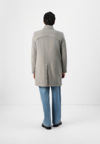 Grau gestrickter Wollmantel mit strukturiertem Kragen, Rückeneinsatz und einem leicht lockeren Schnitt, kombiniert mit hellblauen weit geschnittenen Jeans.