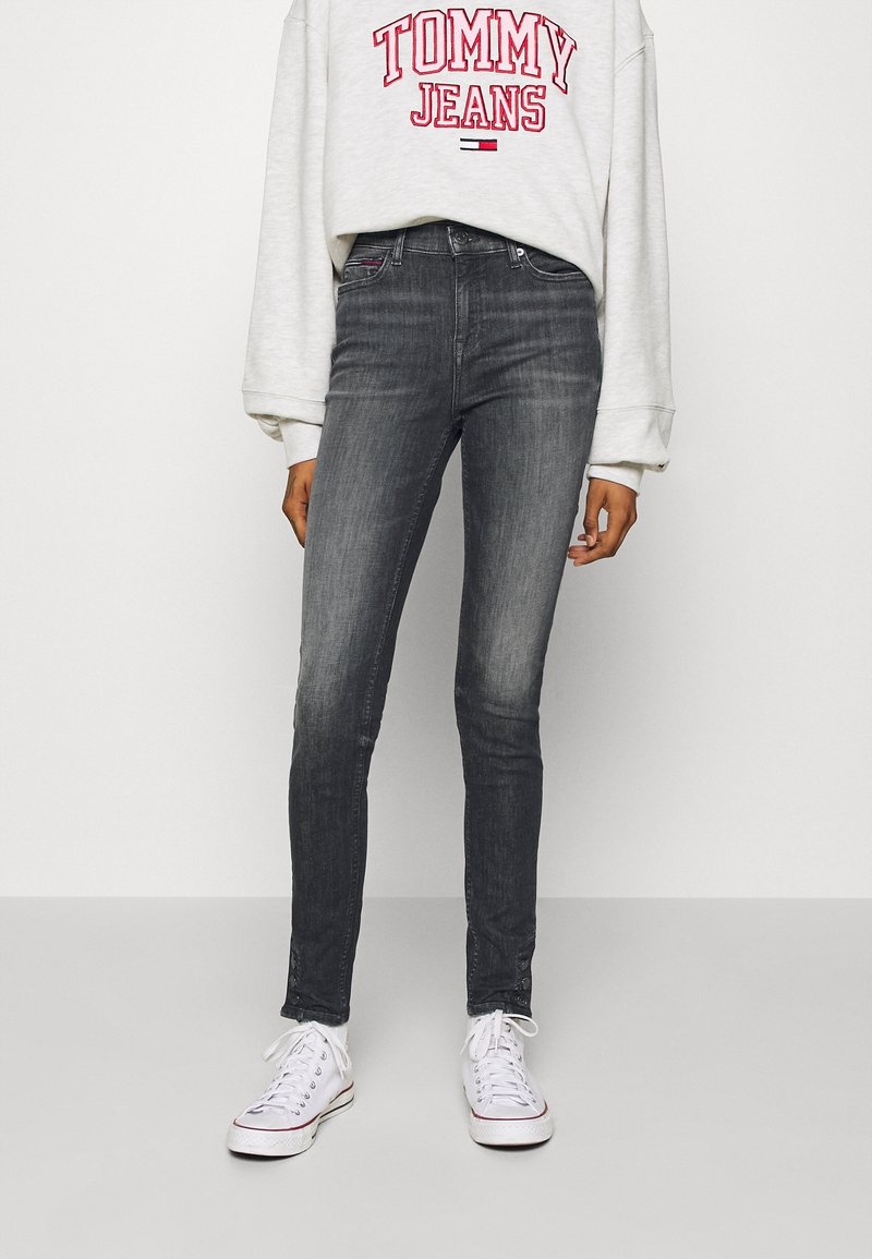 Jeans skinny grigi in tessuto denim, con vita alta e leggera sfumatura. Abbinati a una felpa grigia chiara con scritte rosse. Sneakers bianche.