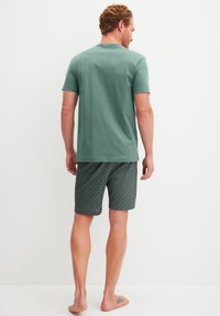 Groene katoenen T-shirt met ronde hals, gecombineerd met donkergekleurde shorts met patronen en geometrische ontwerpen, weergegeven van achteren.