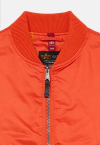 Pomarańczowa kurtka bomberka z prążkowanym kołnierzem, przednim zamkiem i metką z logo. Wykonana z gładkiego materiału syntetycznego w jednolitym kolorze.