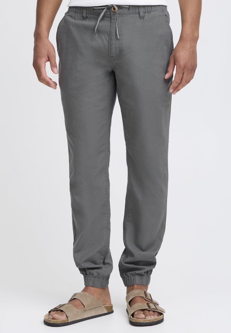 Pantalons de jogging gris avec une taille élastique, une fermeture à cordon et des chevilles resserrées, associés à des sandales à glissière beiges.