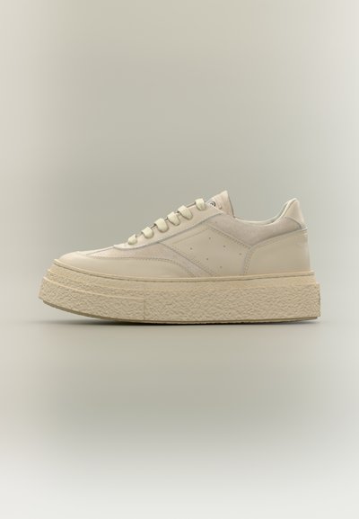 Baskets basses beige avec semelle épaisse texturée, fermeture à lacets et détails en panneaux lisses et en suède sur un fond neutre.