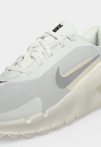Бяла спортна обувка с текстилна материя, бели връзки, сив Nike емблема и плътна, набраздена подметка, видима от страничен ъгъл.