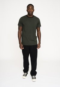 Sortstribet grøn t-shirt med rund hals, parret med sorte bukser og lavtoppede sneakers med hvide såler.