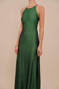 Nő, aki ujj nélküli, földig érő smaragdzöld szaténruhát visel, amelynek nyakrésze pántos, és egy arany karkötőt visel a bal csuklóján.