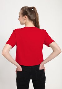T-shirt rouge à manches courtes en coton, avec une coupe décontractée. Le dos présente une texture lisse sans motifs ni accents supplémentaires.