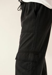 Crne cargo hlače izrađene od izdržljivog materijala, s elastičnom waistband, bočnim džepovima i teksturiranom površinom s vidljivim detaljima šavova.