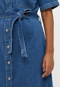 Denim obleka v modri barvi, z kratkimi rokavi, pasom in gumbi spredaj. Gladka tekstura s kontrastnim šivanjem.