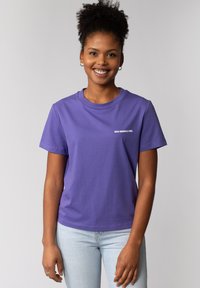 Paarse katoen t-shirt met korte mouwen, ronde hals en een kleine witte tekstprint op de voorkant. Draagt met lichtblauwe spijkerbroek.