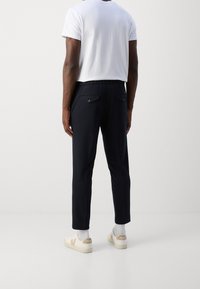 Granatowe casualowe spodnie o dopasowanym kroju, z dwoma tylnymi kieszeniami zapinanymi na guziki, w zestawieniu z białym T-shirtem i jasnymi sneakersami.