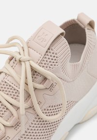 Zapatilla de color rosa claro con parte superior de tejido de punto, cierre con cordones, suela de goma y un logo grabado en la pestaña del talón.