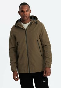 Giacca con cappuccio verde scuro, con zip frontale, tasche laterali e polsini elasticizzati. Il tessuto è liscio, con una sottile trama e linee pulite.