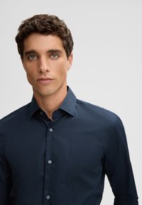 Marineblauw knoopshirt met een gestructureerde kraag, lange mouwen en een gladde textuur. Beschikt over een subtiele glans en een effen ontwerp.