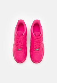 Des baskets Nike Air Force 1 en cuir rose avec une surface lisse, une boîte à orteils arrondie, des perforations pour la respirabilité et des lacets plats.