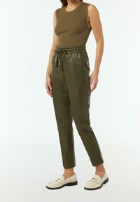 Haut sans manches côtelé vert olive associé à un pantalon de jogging en faux cuir lisse et fuselé avec une ceinture élastique, et des mocassins crème.