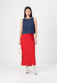 Donkerblauw denim crop top gecombineerd met een lange rode rok. Witte sneakers en een kleine witte handtas maken de outfit compleet.