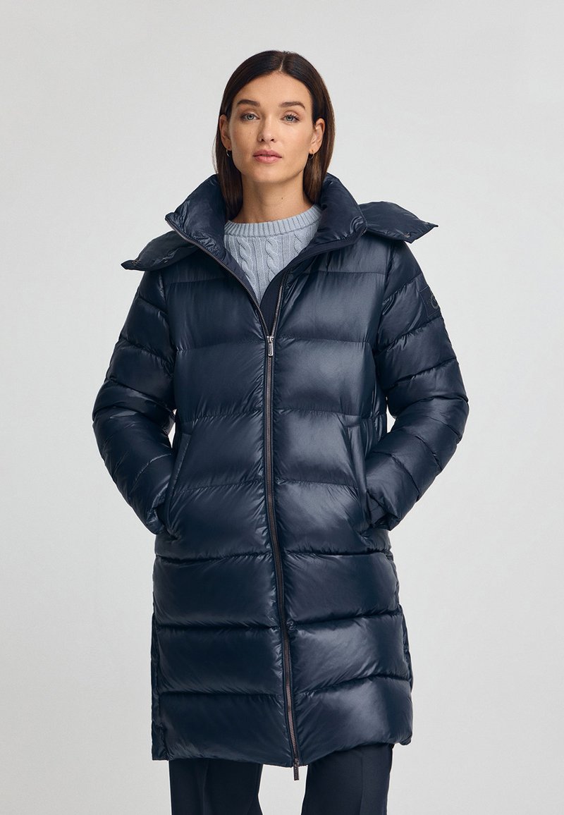 Mörkblå vinterjacka med dragkedja framtill, hög krage, kviltat mönster och sidofickor. Slät, glänsande yta.