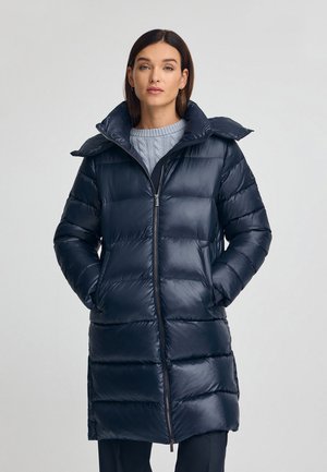 Abrigo acolchado azul marino con cremallera frontal, que presenta un cuello alto, patrón acolchado y bolsillos laterales. Textura suave y brillante.