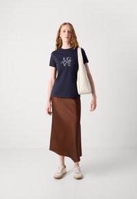 Navy cotton t-shirt with "LOVE" graphic, paired with brown satin midi skirt. Model holds a white bag, wearing beige sneakers.