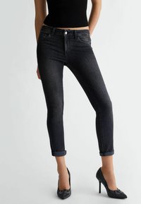 Jeans negros ajustados con un talle medio, con detalles de diamantes de imitación en la parte delantera y dobladillos enrollados en los tobillos.