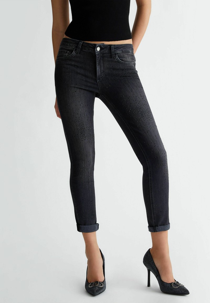 Jeans negros ajustados con un talle medio, con detalles de diamantes de imitación en la parte delantera y dobladillos enrollados en los tobillos.