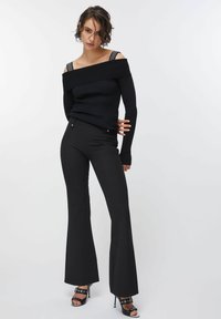 Črna rebrasta majica brez ramen s dekorativnimi naramnicami, kombinirana s črnimi razširjenimi hlačami in črnimi sandali z visokimi petami.