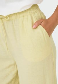 Lichtgele, loszittende broek met een elastische tailleband en trekkoord, voorzien van een zijzak en een zachte, gestructureerde stof.