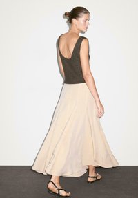 Lys beige, flydende nederdel med en tekstureret mørk top. Nederdelen har en lang A-formet silhuet, og toppen har en bred scoop-ryg. Sorte sandaler.