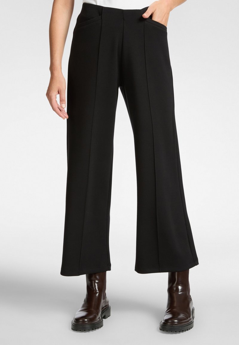 Zwarte wijde broek met een gladde textuur, voorzien van opgestikte zakken en verticale naden, gecombineerd met een paar bruine enkellaarzen.