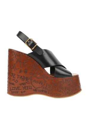 Sandale compensée en cuir noir avec une semelle plateforme marron ornée d’écritures style graffiti et une bride de cheville avec boucle dorée.