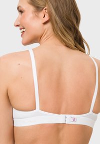 White bra with adjustable straps and hook closure at the back. Soft fabric with subtle brand logo near the fastening. Smooth texture.
