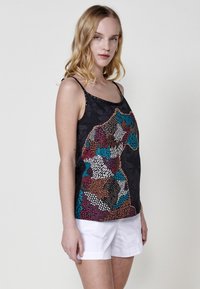 Must have mustris püstolijakiga must tank top, millel on mitmevärvilised tekstuurilised mustrid, mis kujutavad looma kuju, ja mis on kaunistatud väikeste nupukestega rihmade peal. Kanda koos valgete lühikestega.