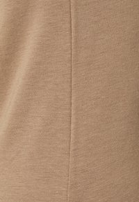 Un tissu beige côtelé avec une texture lisse présente une couture verticale. Le matériau semble léger et élastique, idéal pour des vêtements ajustés.