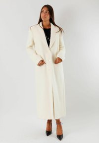 Lungo cappotto bianco in lana con rever, due bottoni, tasche laterali e taglio dritto. Texture liscia, lunghezza al ginocchio e dettagli di design minimalisti.