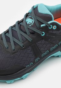 Svart og teal fottur sko med et teksturert mesh-overdel, Gore-Tex merkevare, og slitesterk gummisåle. Har kontrasterende blå snøringer og logo.