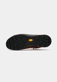 Suola di scarpa in gomma nera con scanalature profonde, caratterizzata da un logo Vibram giallo e accenti arancioni lungo i bordi per una maggiore aderenza e durabilità.