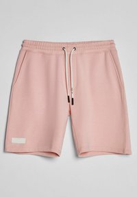 Shorts en coton rose clair avec taille élastique, cordons blancs, poches latérales et ourlet cousu sur un fond gris clair uni.