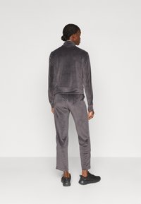Tuta in velour grigia con giacca con zip e pantaloni con vita elastica. Texture liscia, silhouette aderente, lucentezza sottile e accenti neri.