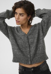 Harmaa neulecardigan, jossa on syvä V-pääntie, ribbatut helmat ja nappidetaljit edessä. Pehmeä rakenne ja löysä istuvuus, lyhyempi pituus.