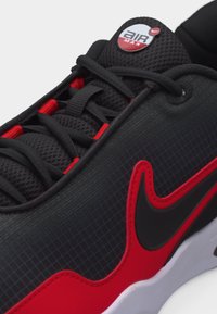 Κοντινή λήψη της περιοχής των κορδονιών και της πλευράς ενός μαύρου και κόκκινου αθλητικού παπουτσιού Nike Air Max, με μαύρο λογότυπο Swoosh με κόκκινο περίγραμμα και γλώσσα από πλέγμα.