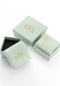 Quadratische mintgrüne Boxen aus Papier mit goldener Schrift. Eine Box ist geöffnet und zeigt ein schwarzes Innere. Der Text enthält Marken- und Recyclinginformationen.