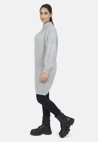 Lysegrå strikket sweaterkjole med høj hals, ribbet struktur, lange ærmer og slidser i siderne, parret med sorte snørebåndsbokse.