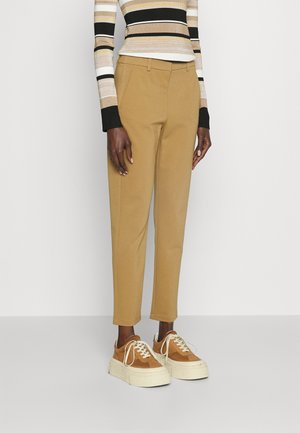Personne portant un pantalon beige fuselé, un haut à manches longues rayé et des baskets à plateforme beige, debout devant un fond uni.